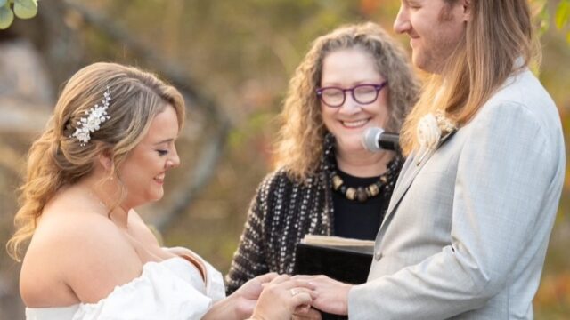 Bride places ring on groom’s finger during joyful outdoor wedding ceremony officiated by NJ Vows Now. Photo by Gary Flom Photography.