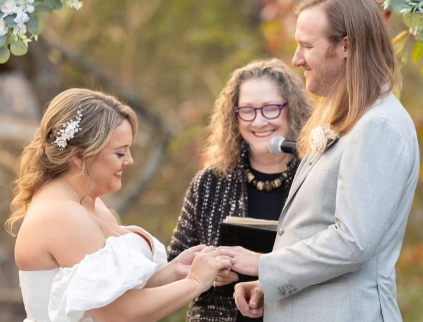 Bride places ring on groom’s finger during joyful outdoor wedding ceremony officiated by NJ Vows Now. Photo by Gary Flom Photography.