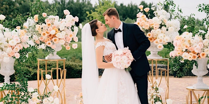 A bride and groom share a tender moment surrounded by lush peach and white floral arrangements at their wedding ceremony.