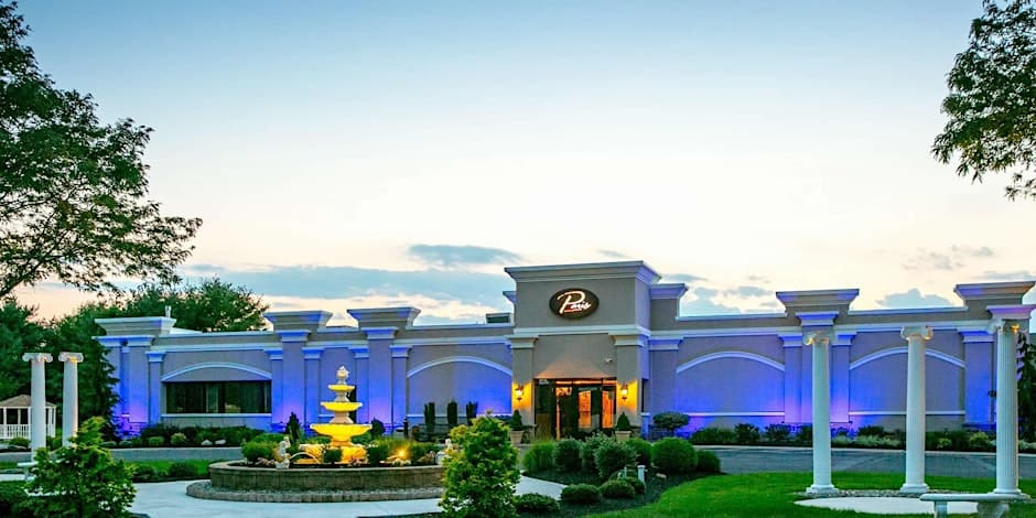 The exterior of Paris Caterers at dusk, showcasing its elegant facade with blue uplighting, a grand fountain, and classic white columns.
