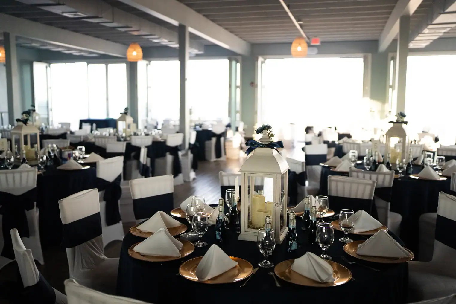 Elegant coastal banquet room set for a wedding reception with navy and white linens, gold chargers, and lantern centerpieces at The Ocean View Restaurant.