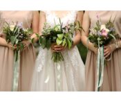 Three women in blush dresses holding lush, garden-style wedding bouquets with greenery and pastel flowers.