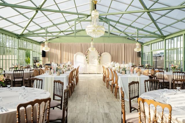 Light-filled glass garden-style reception space with chandeliers and round tables, representing DIY-friendly wedding venues NJ.