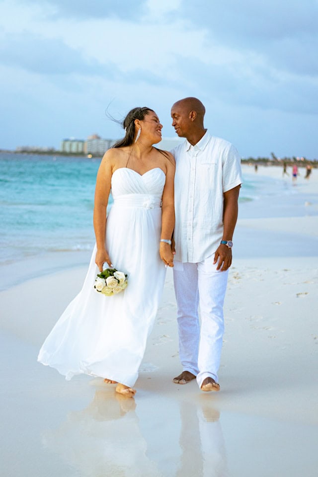 Black bride and groom embracing on the beach, with the bride wearing a chic bridal gown for a beach wedding.
